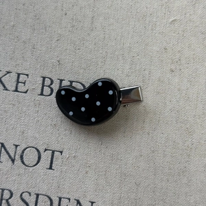 Detail shot of a black heart hair clip with white polka dots on a beige canvas surface