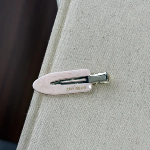 Vue macro d'une barrette en acétate rose marbré avec logo doré sur tissu beige