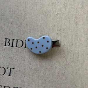 Close-up of blue polka dot hair clip with silver metal grip on beige fabric