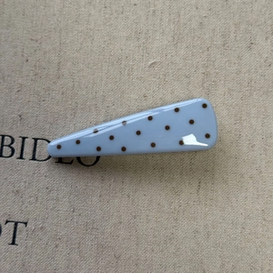 Detailed macro view of light blue triangular hair clip with dark brown polka dots