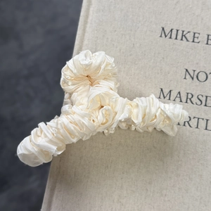 Elegant cream pleated satin hair claw clip for women on a book with soft lighting