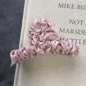 Detailed view of pink pleated satin fabric wrapping the metal claw clip on a book