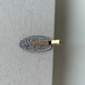 Detailed view of silver glitter oval hair clip with gold metal base on fabric