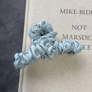 Close-up of light blue pleated satin fabric wrapping a shark hair clip on a book