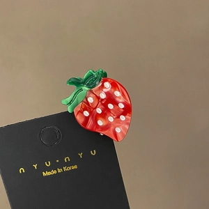 Detailed macro view of a red strawberry-shaped acetate hair clip on a black display card