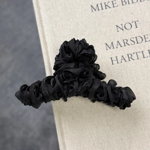 Detail of elegant black pleated fabric rose hair claw clip on an aesthetic book background