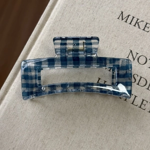 Dettaglio della pinza per capelli a quadretti blu con molla dorata su un libro