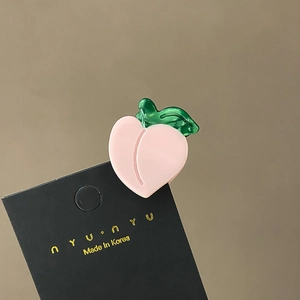 Detail of a peach-shaped acetate hair claw clip with green leaf on a display card