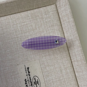 Detail einer lila karierten Haarklammer mit Herzkristall auf einem beigen Stofftablett