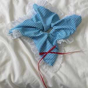 Gros plan d'un chouchou à carreaux bleus avec bordure en dentelle blanche et nœud rouge