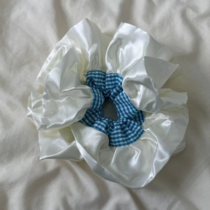 Détail macro d'un chouchou double couche en satin crème avec des motifs à carreaux bleus