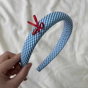 Détail d'un serre-tête à carreaux bleus avec nœud rouge et étiquette gravée LOVE