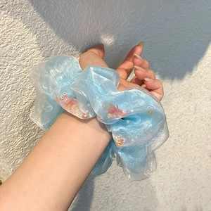 Chouchou en organza bleu clair avec perles colorées, porté avec style au poignet d'une femme