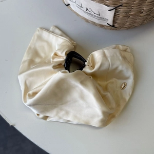 Close-up of cream satin bow hair claw clip with elegant golden brand plaque detail
