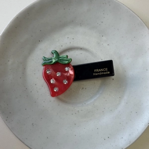 Sweet strawberry acetate hair clip with rhinestones on a minimalist ceramic plate