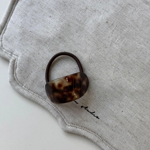 Detail of tortoiseshell acetate hair tie with dark brown elastic band on linen