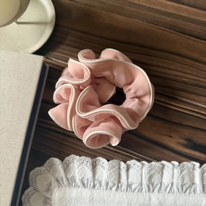 Vue détaillée du chouchou en mousseline rose avec passepoil blanc sur fond en bois