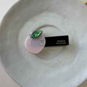 Detailed top view of a peach-shaped acetate hair clip with rhinestones on a grey tray
