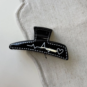 Gros plan sur une pince à cheveux noire avec motif battement de cœur et couture