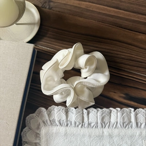 Vue détaillée d'un chouchou en satin blanc plissé sur une table avec des accessoires