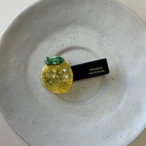 Detailed macro of a yellow fruit hair clip featuring rhinestones and handmade gold lettering
