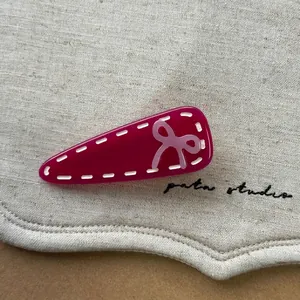Détail macro d'une pince à cheveux fuchsia avec coutures blanches et petit nœud