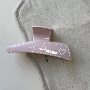 Détail de la pince à cheveux trapèze rose mat avec motif cœur blanc et couture