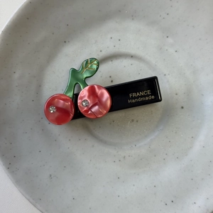 Detail of red cherry hair clip with rhinestones and gold leaf texture on a ceramic dish