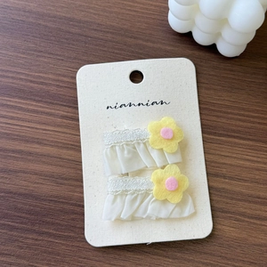 Detail of two lace floral hair clips with yellow fabric flowers on a paper card