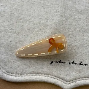 Détail de la pince à cheveux crème avec nœud en résine orange et finition grain de bois