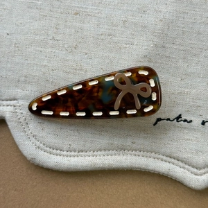 Détail de la pince à cheveux écaille avec nœud marron et couture blanche sur toile