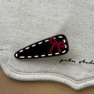 Vue détaillée d'une pince noire en goutte d'eau avec nœud rouge sur toile beige
