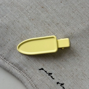 Minimalist yellow popsicle-shaped metal hair clip on a neutral linen texture background