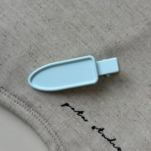Close-up of light blue capsule-shaped hair clip with spring duckbill clamp on fabric