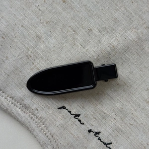 Close-up of a glossy black metal duckbill hair clip on a natural beige linen background