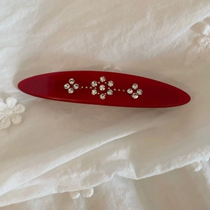 Macro detail of red oval acetate hair clip with sparkling rhinestone flower patterns