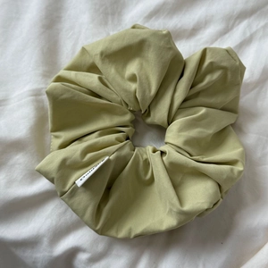 Close-up of olive green ribbed scrunchie with woven label on soft white linen background