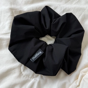 Detail of a black pleated scrunchie with Oulifang logo tag on a white fabric background