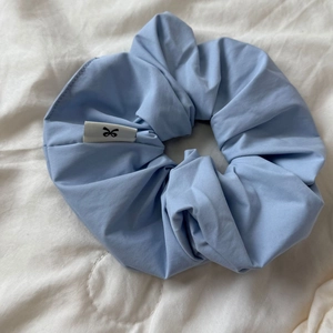 Detailed view of light blue cotton scrunchie with twill texture and small bow logo tag