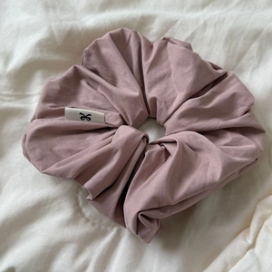 Macro shot of dusty pink satin scrunchie with a minimalist bow logo label on soft fabric