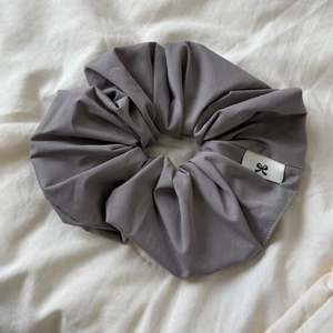 Detail view of a grey scrunchie with twill texture and a small bow logo tag