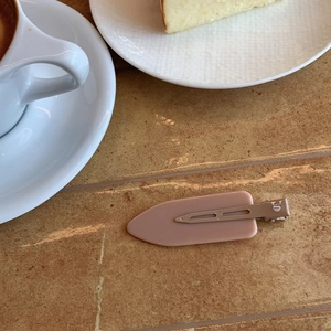 Close-up of matte pink geometric hair clip on a marble tabletop with coffee background