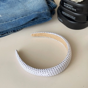 Detailed close-up of a wide padded headband featuring classic black polka dots on white fabric