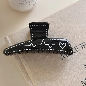 Vue détaillée d'une pince à cheveux noire avec motif graffiti cœur sur fond beige