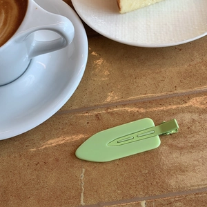 Close-up of pale green matte duckbill hair clip on warm marble background