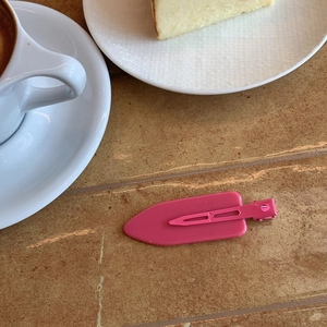 Pink teardrop hair clip on a wooden table with a coffee cup and sweet cake decor