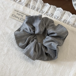 Détail d'un chouchou gris rayé en lin posé sur un tissu avec bordure en dentelle