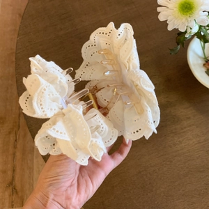 Detailed close-up of a white lace flower hair claw clip with pearls on a wooden desk