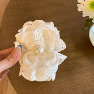 Close-up of white lace flower hair clip with central pearl and layered texture