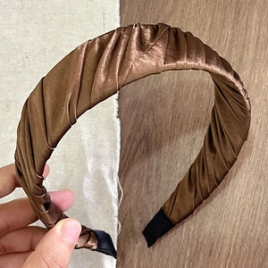 Close-up of brown satin pleated headband with fine fabric texture and ribbing detail